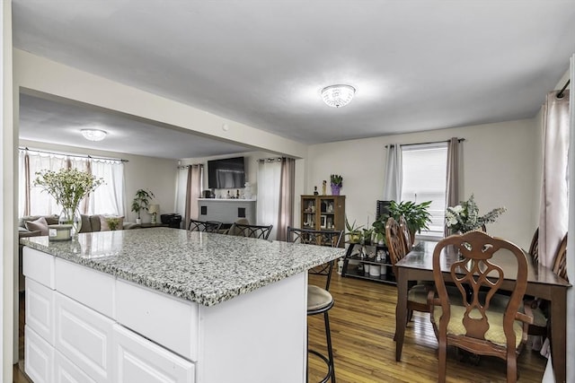 kitchen with a breakfast bar, white cabinetry, open floor plan, dark wood-style floors, and light stone countertops