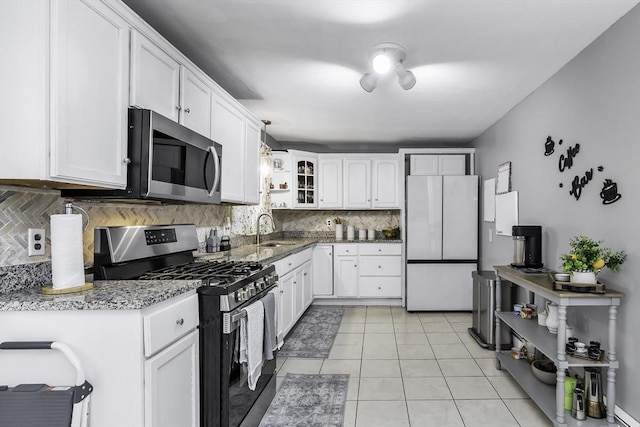 kitchen featuring stainless steel appliances, a sink, tasteful backsplash, white cabinetry, and light stone counters