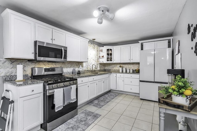 kitchen with appliances with stainless steel finishes, white cabinetry, decorative backsplash, dark stone counters, and a sink