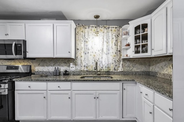 kitchen featuring stainless steel appliances, a sink, white cabinetry, decorative backsplash, and dark stone countertops