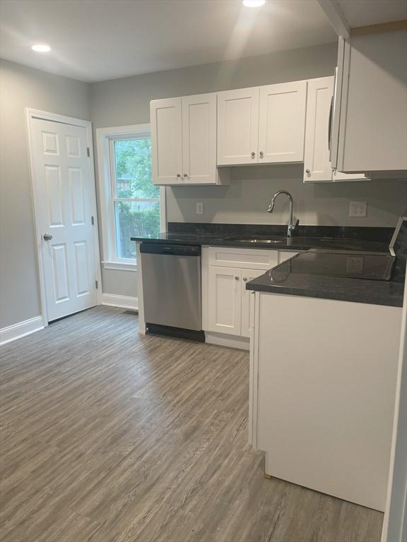 15 Forest St, Whitman, MA 02382 - kitchen featuring stainless steel dishwasher, a sink, white cabinets, wood finished floors, and dark countertops