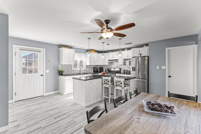 kitchen with tasteful backsplash, a center island, under cabinet range hood, white cabinets, and stainless steel appliances