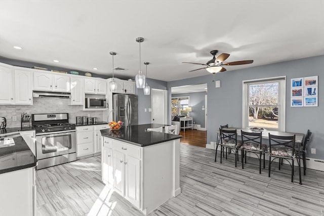 kitchen featuring white cabinets, under cabinet range hood, appliances with stainless steel finishes, dark countertops, and tasteful backsplash