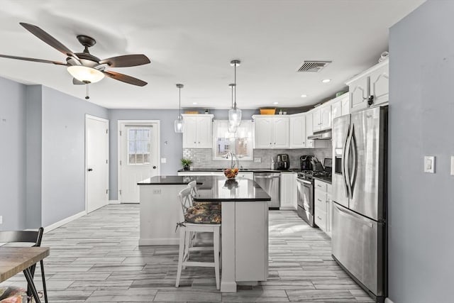 kitchen with dark countertops, visible vents, a kitchen island, under cabinet range hood, and stainless steel appliances