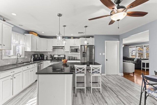 kitchen featuring dark countertops, appliances with stainless steel finishes, a kitchen island, and a sink