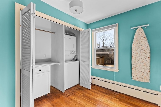 laundry area with a baseboard heating unit, laundry area, stacked washer / dryer, and light wood-style flooring