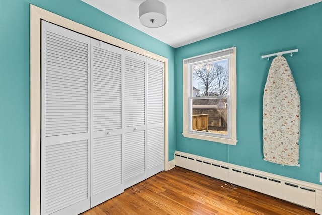 unfurnished bedroom with wood finished floors, a closet, and baseboard heating