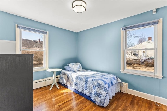 bedroom featuring a baseboard heating unit, baseboards, and wood finished floors