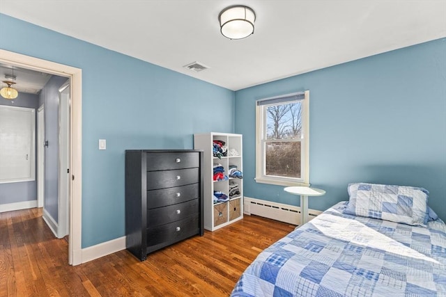 bedroom with visible vents, wood finished floors, baseboards, and a baseboard heating unit