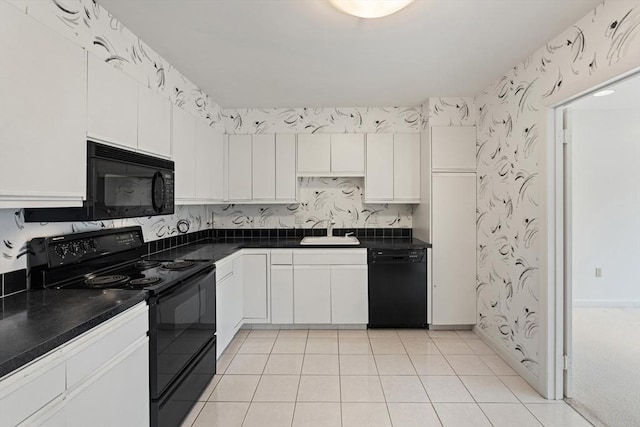 kitchen with black appliances, a sink, dark countertops, white cabinets, and wallpapered walls