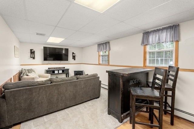 living area with a paneled ceiling, light wood-type flooring, and a baseboard heating unit