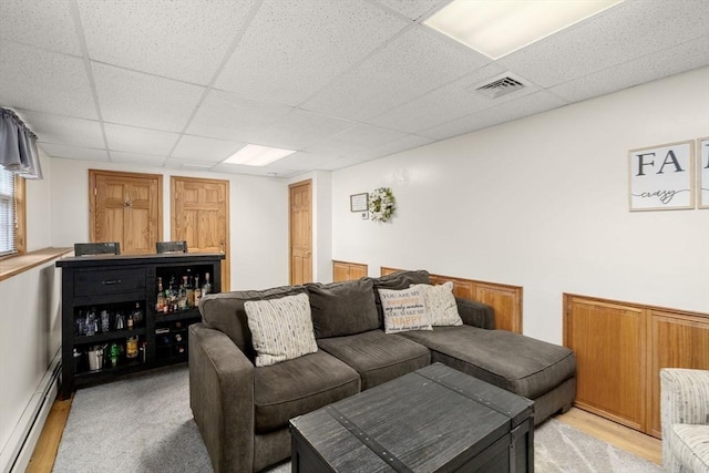 living room featuring a baseboard radiator, light wood-style flooring, and a drop ceiling