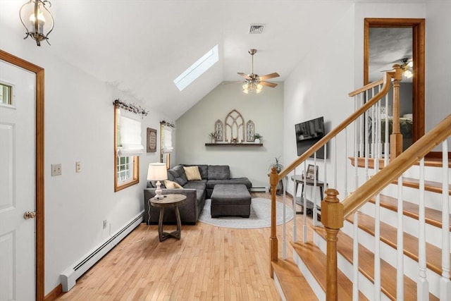 living area featuring a baseboard heating unit, light wood-style flooring, ceiling fan, a skylight, and stairway