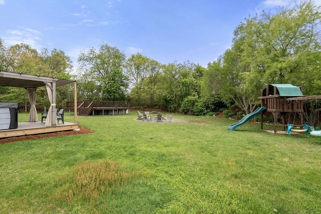 view of grassy yard featuring a deck, an outdoor fire pit, a playground, and view of scattered trees