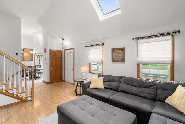 living area featuring a chandelier, light wood-style floors, stairway, a skylight, and high vaulted ceiling