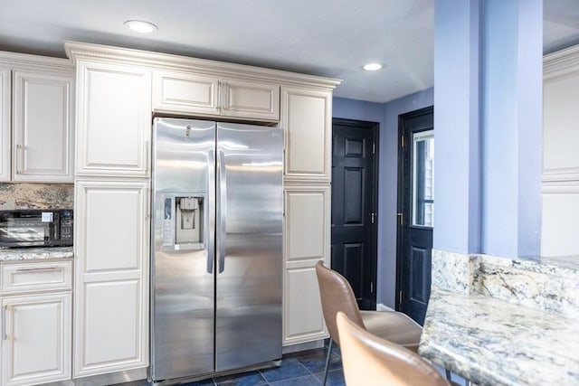 kitchen with black microwave, recessed lighting, light stone countertops, and stainless steel fridge with ice dispenser