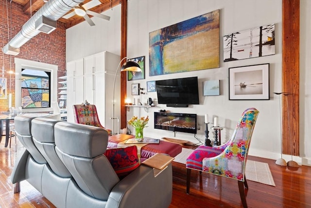 49 Munroe St Unit 405, Lynn, MA 01901 - living room featuring a towering ceiling, a glass covered fireplace, wood finished floors, a ceiling fan, and brick wall