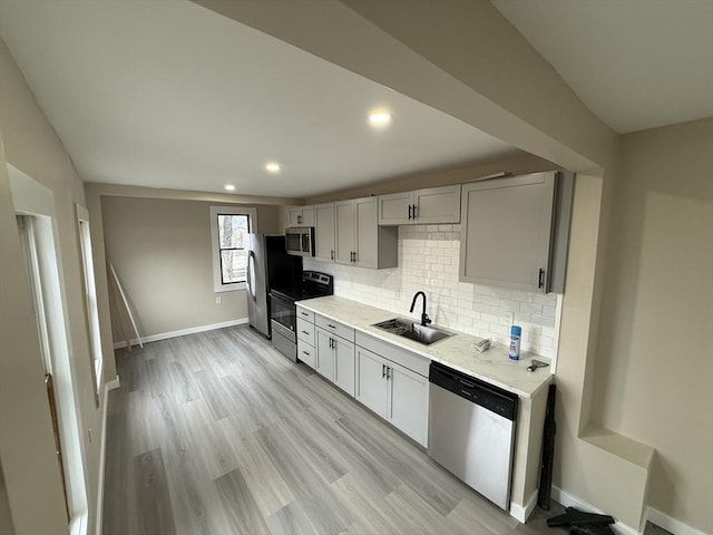 kitchen with appliances with stainless steel finishes, a sink, light countertops, baseboards, and decorative backsplash