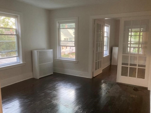 empty room featuring dark hardwood / wood-style flooring, radiator heating unit, and a wealth of natural light