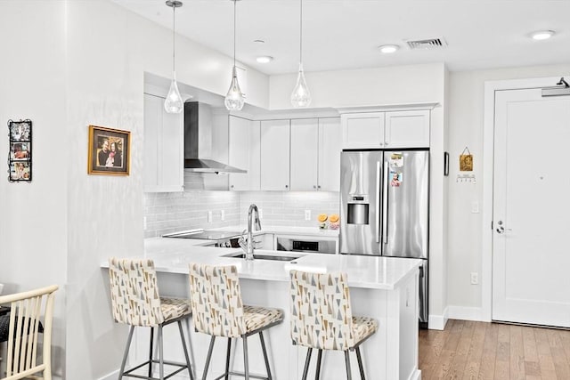 kitchen with wall chimney exhaust hood, a sink, a peninsula, and light countertops