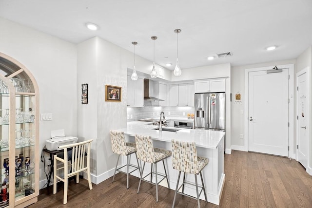 kitchen featuring wall chimney exhaust hood, stainless steel fridge with ice dispenser, a sink, light countertops, and white cabinetry