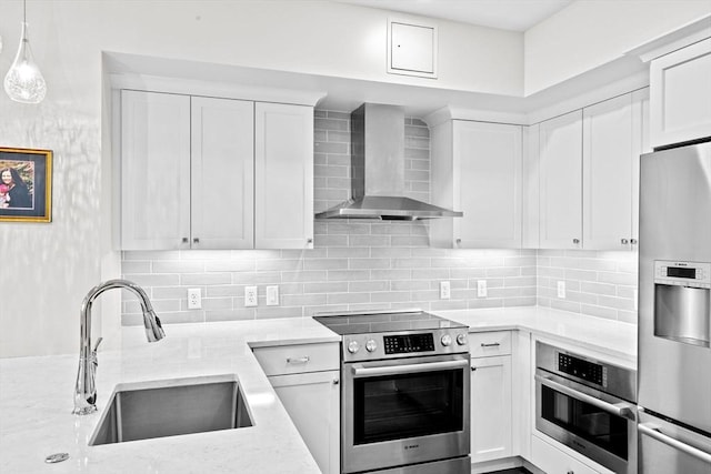 kitchen featuring wall chimney range hood, stainless steel appliances, a sink, light stone counters, and white cabinetry