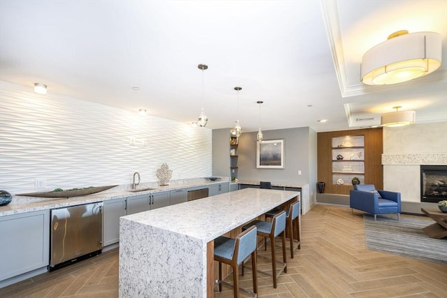 kitchen with gray cabinets, light stone countertops, a kitchen breakfast bar, a kitchen island, and a sink