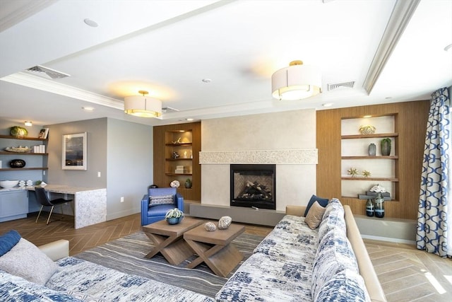 living area with built in features, baseboards, a tray ceiling, crown molding, and a fireplace