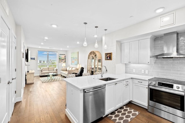 kitchen with wall chimney exhaust hood, a sink, appliances with stainless steel finishes, a peninsula, and light countertops