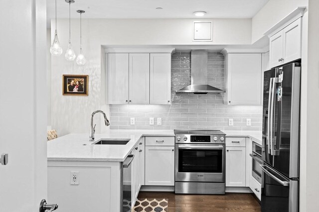 kitchen with stainless steel appliances, wall chimney exhaust hood, a sink, a peninsula, and dark wood-type flooring