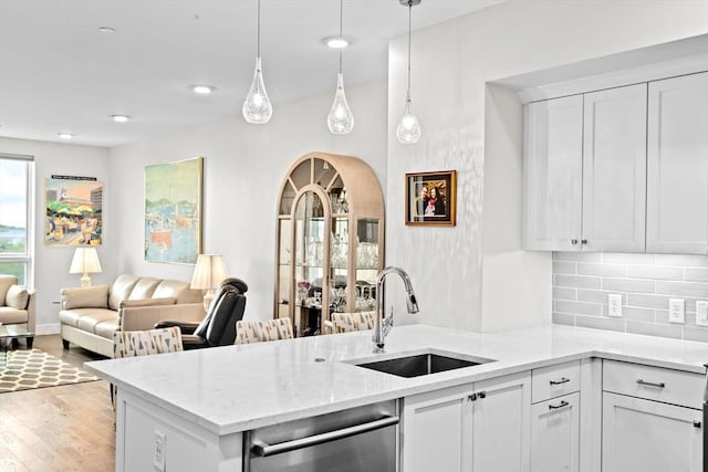 kitchen featuring a sink, a peninsula, stainless steel dishwasher, decorative backsplash, and open floor plan