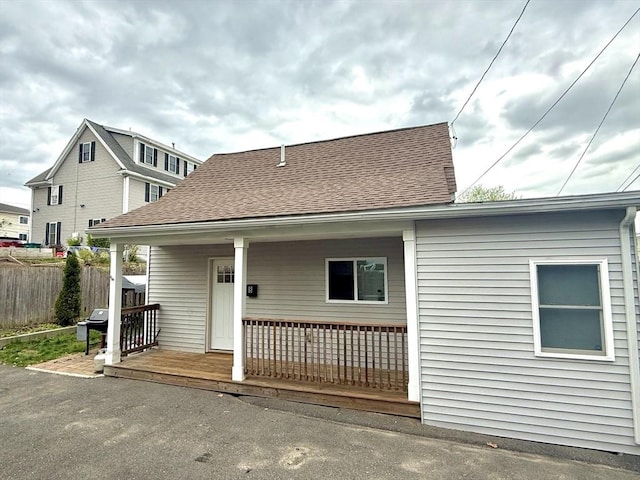view of front of home with fence, roof with shingles, and covered porch