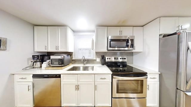 kitchen featuring appliances with stainless steel finishes, a sink, white cabinets, and tasteful backsplash