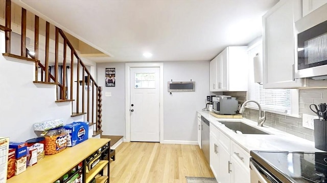 kitchen with a sink, backsplash, light wood-style flooring, baseboards, and appliances with stainless steel finishes