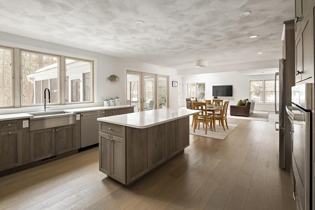 kitchen featuring a kitchen island, hardwood / wood-style floors, light countertops, stainless steel dishwasher, and a sink