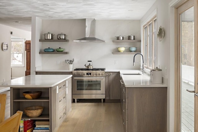 kitchen with a sink, wall chimney range hood, stainless steel gas range oven, and open shelves