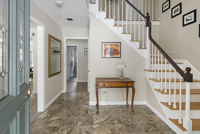 foyer entrance with stairway and baseboards