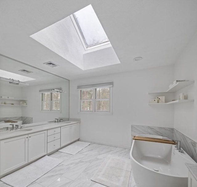 bathroom featuring double vanity, a skylight, marble finish floor, a freestanding bath, and a sink