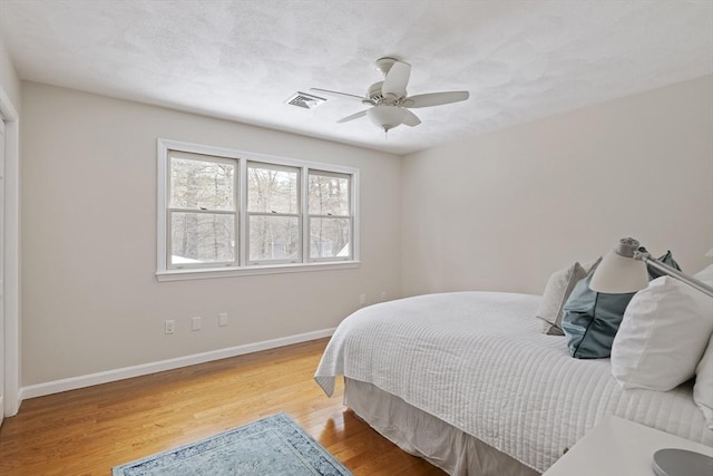 bedroom featuring ceiling fan, light wood finished floors, visible vents, and baseboards