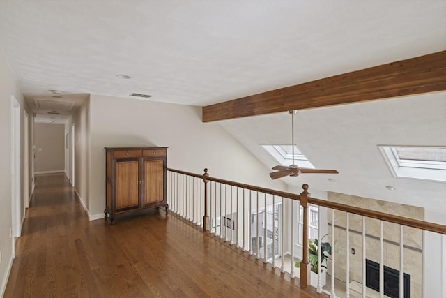 hallway featuring lofted ceiling with skylight, baseboards, visible vents, and dark wood finished floors