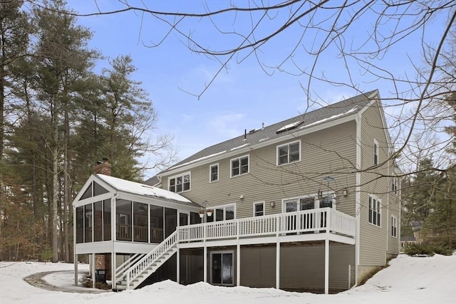 snow covered house featuring stairway, a sunroom, a chimney, and a deck