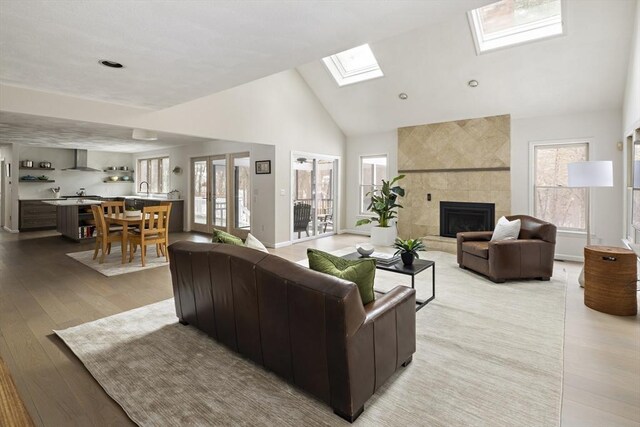 living area featuring high vaulted ceiling, a skylight, wood finished floors, a fireplace, and baseboards