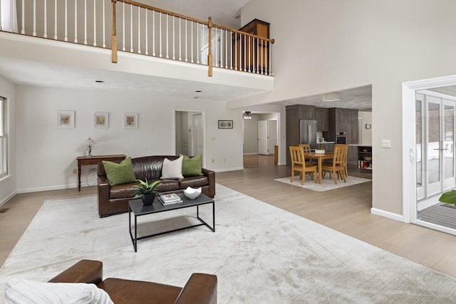 living area featuring a towering ceiling, light wood-style flooring, and baseboards