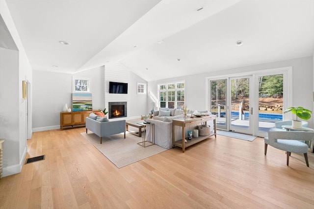 living area with baseboards, visible vents, lofted ceiling, light wood-style flooring, and a lit fireplace