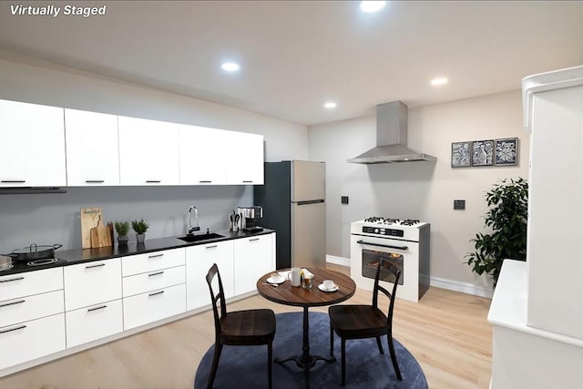 kitchen with wall chimney range hood, white gas range, freestanding refrigerator, modern cabinets, and a sink