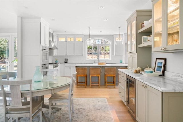 kitchen featuring pendant lighting, light wood-style flooring, beverage cooler, white cabinets, and glass insert cabinets