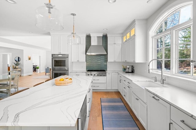 kitchen with a sink, backsplash, white cabinetry, stainless steel appliances, and wall chimney exhaust hood