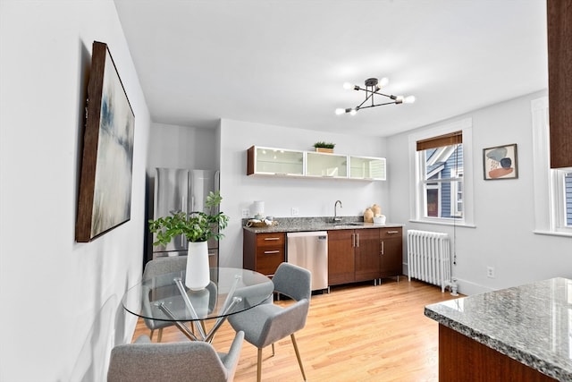 kitchen featuring radiator heating unit, appliances with stainless steel finishes, an inviting chandelier, dark stone counters, and light hardwood / wood-style floors