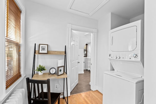 washroom with hardwood / wood-style floors, stacked washer / dryer, and radiator