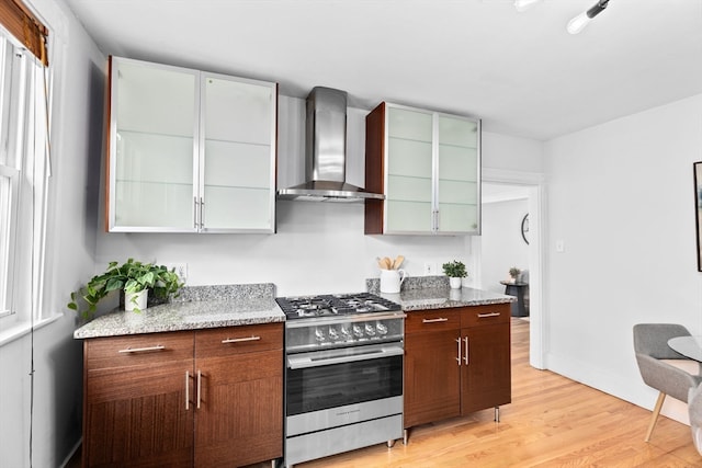 kitchen featuring stainless steel range, wall chimney exhaust hood, light hardwood / wood-style flooring, and light stone counters